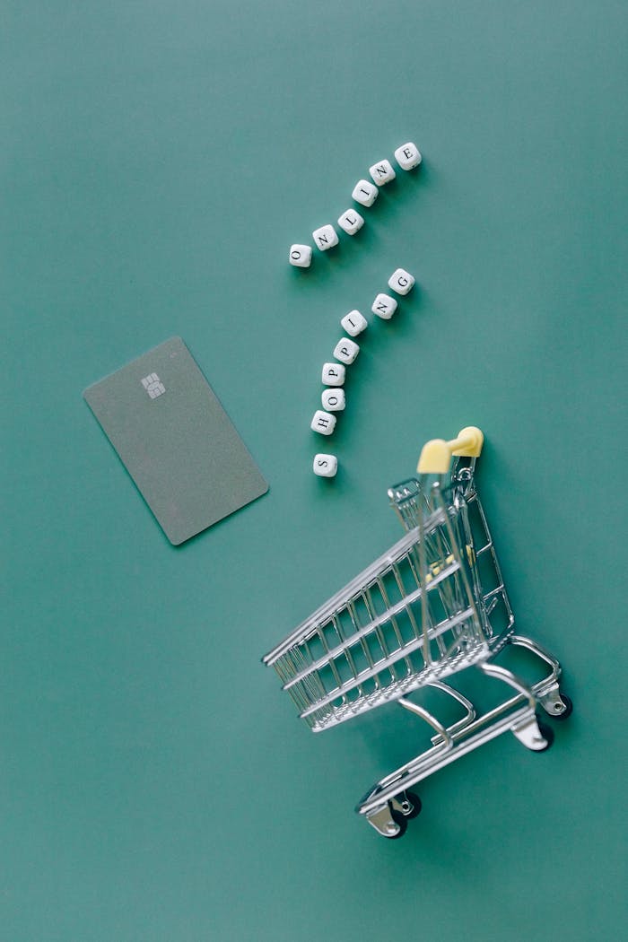 A conceptual image featuring a mini shopping cart, credit card, and letter blocks spelling online shopping on a green background.